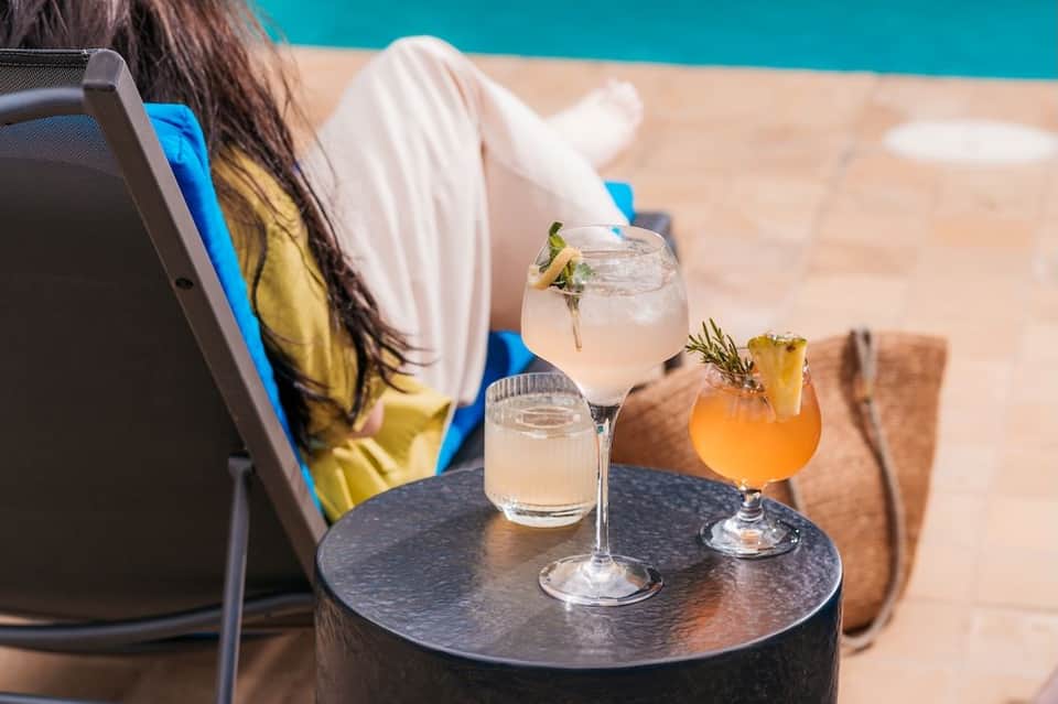Woman relaxing in lounge chair holding cocktails poolside with turquoise water in background