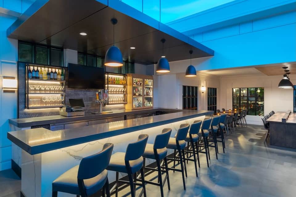 Modern hotel bar interior with blue lighting, illuminated shelving, and marble counter seating
