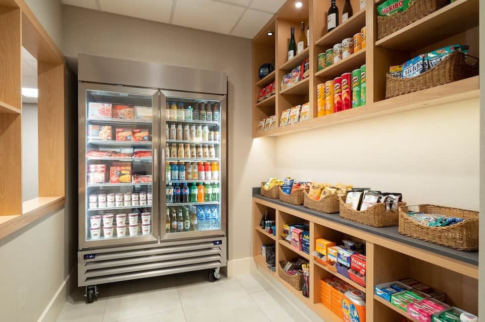 Modern pantry with refrigerated beverage display, wooden shelving, and organized snacks and supplies