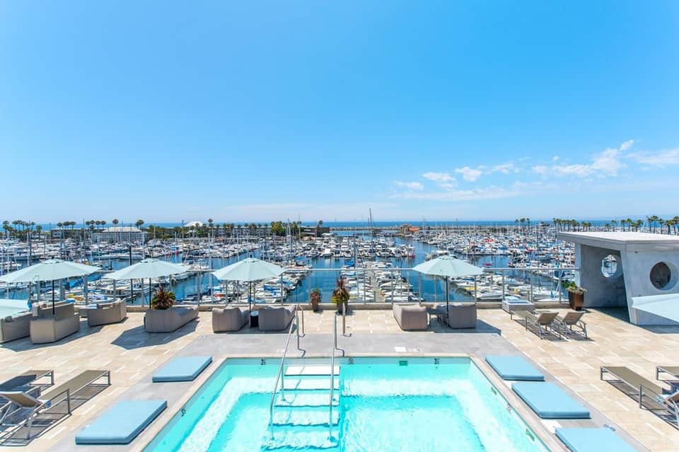 Expansive rooftop pool overlooking marina with multiple sailboats, white umbrellas, and ocean views
