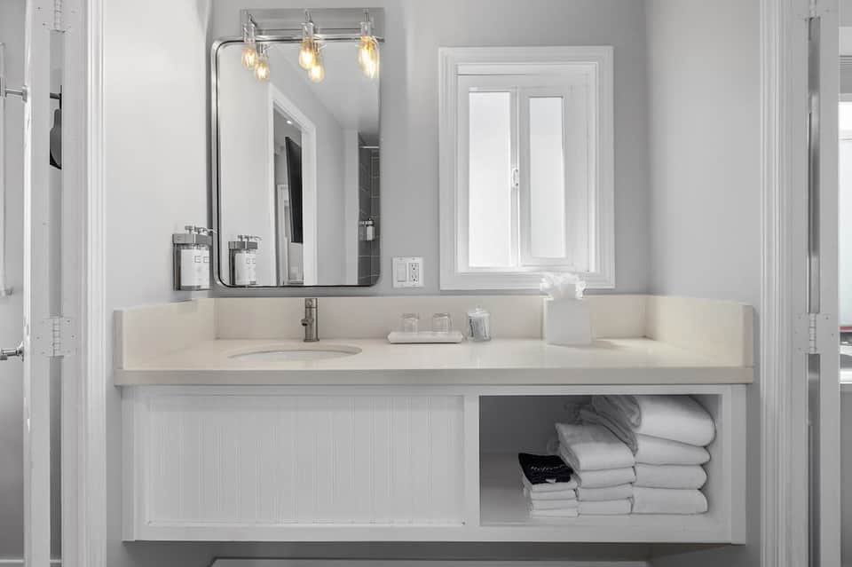 Modern white bathroom with long vanity, pendant lights, large mirror, and shelving with towels