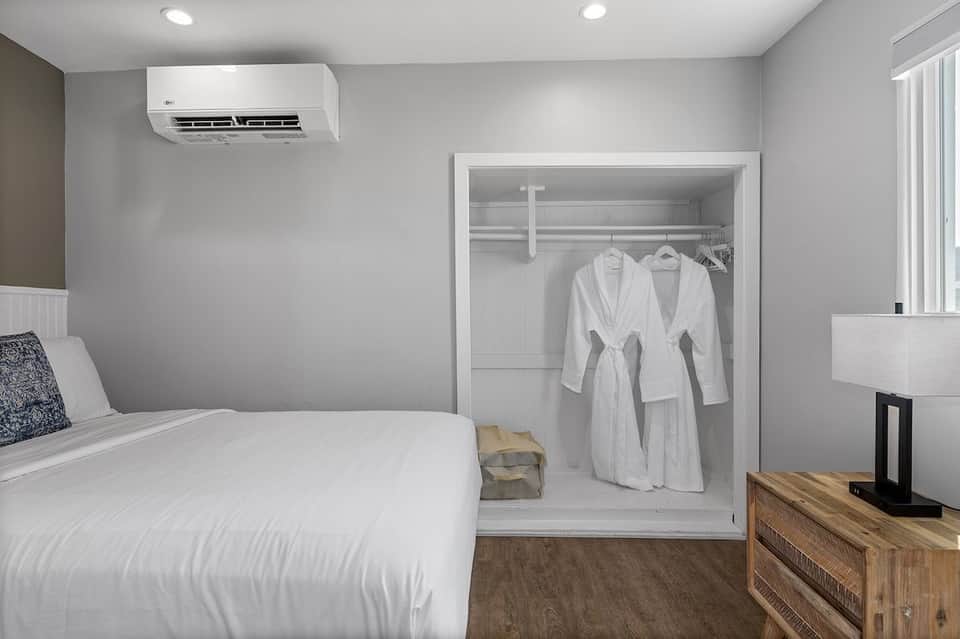 Hotel bedroom with queen bed, open walk-in closet with white robes, and air conditioning unit