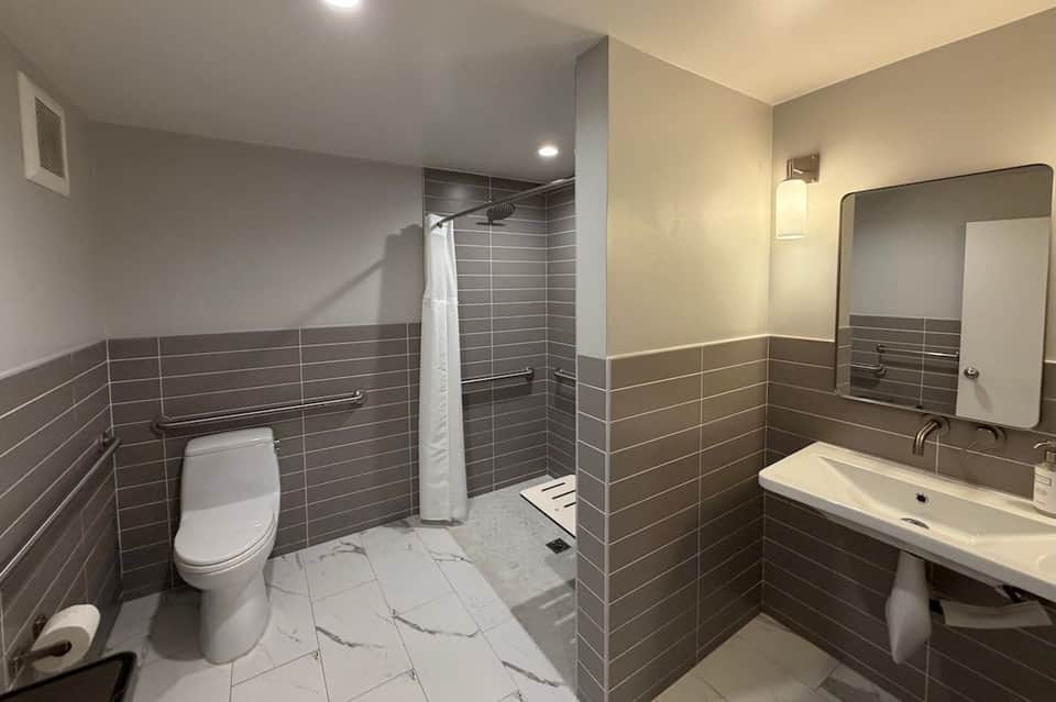 Bathroom with gray tile walls, white sink vanity, toilet, and large mirror