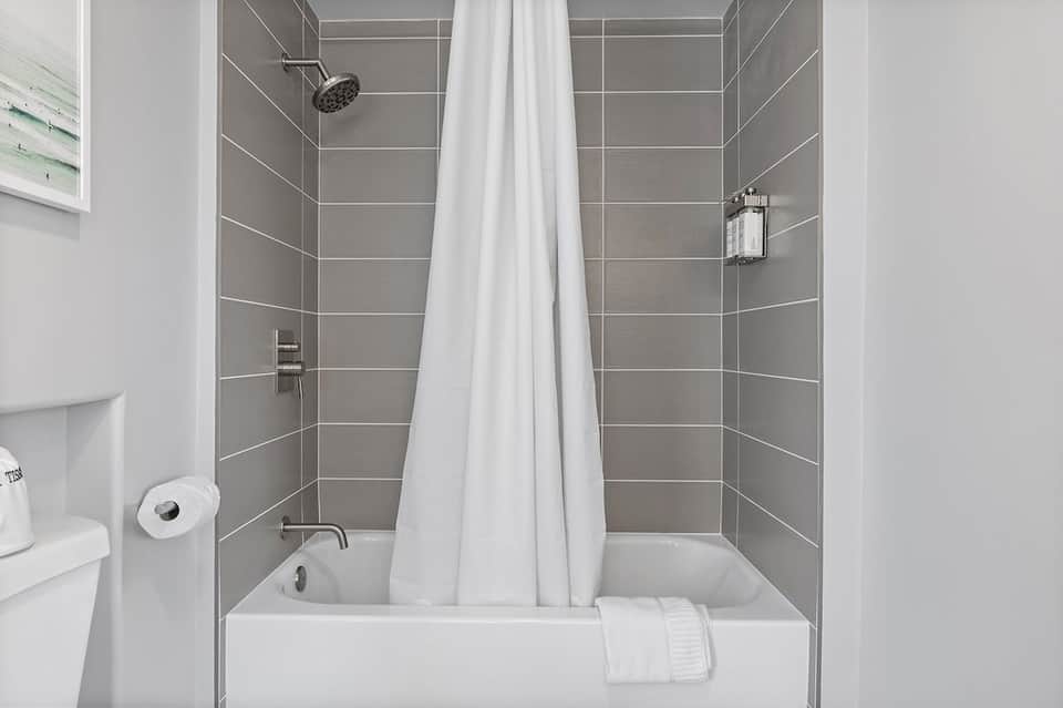 Contemporary bathroom with gray tile walls, white soaking tub, and shower enclosure