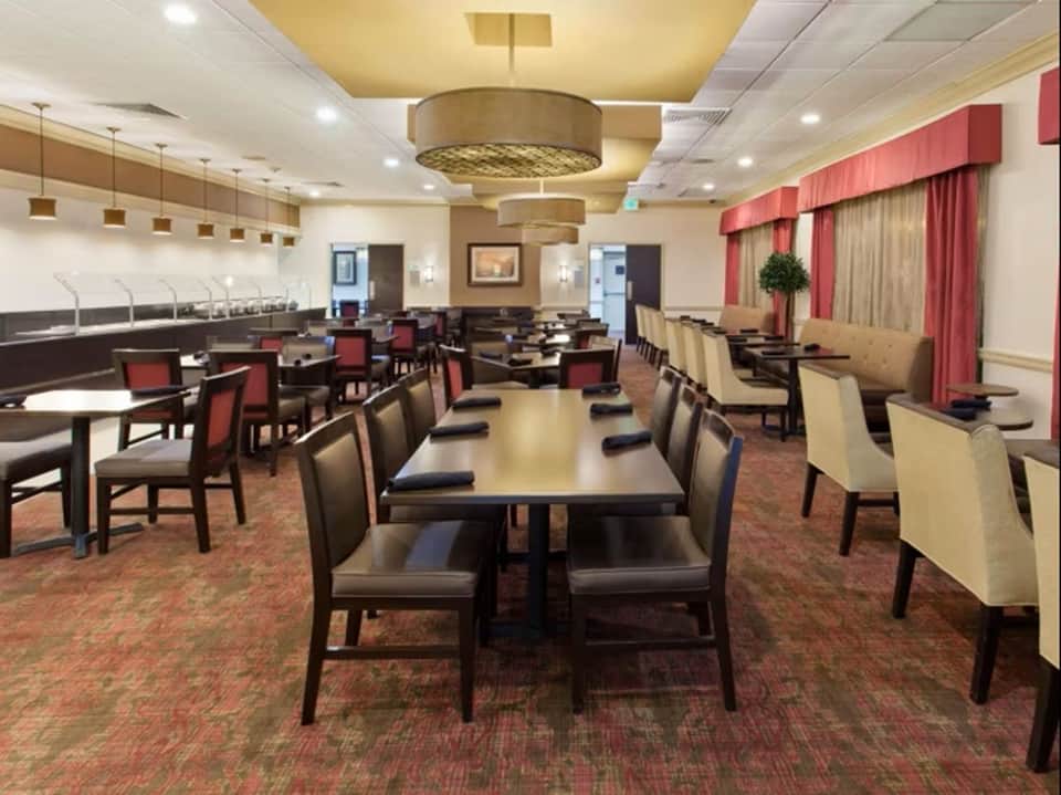 Hotel breakfast or dining area with multiple tables, red chairs, and decorative ceiling fixtures