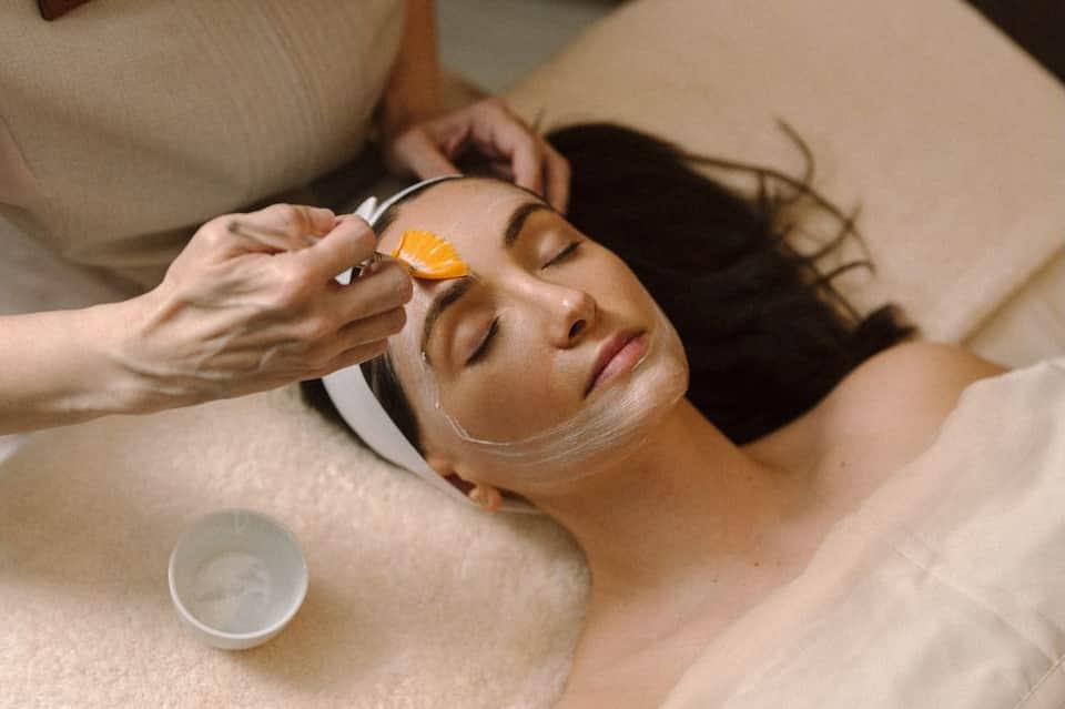 Spa therapist applying golden facial mask to relaxed client during professional skincare treatment