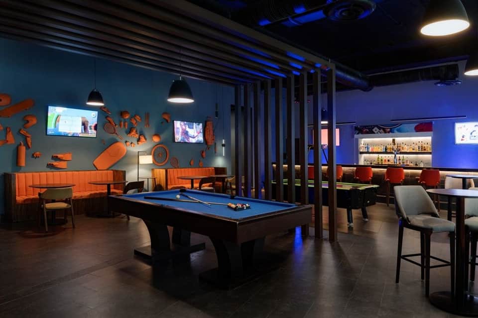 Upscale game room with blue lighting, pool table, bar seating, and entertainment venue