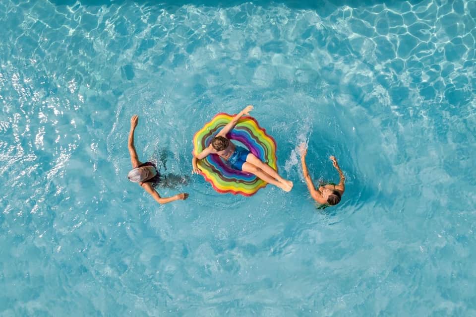 Aerial view of swimmers with colorful float in crystal-clear turquoise pool water