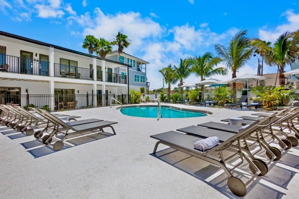 Modern apartment building with curved pool, lounge chairs, and white umbrellas in sunny courtyard