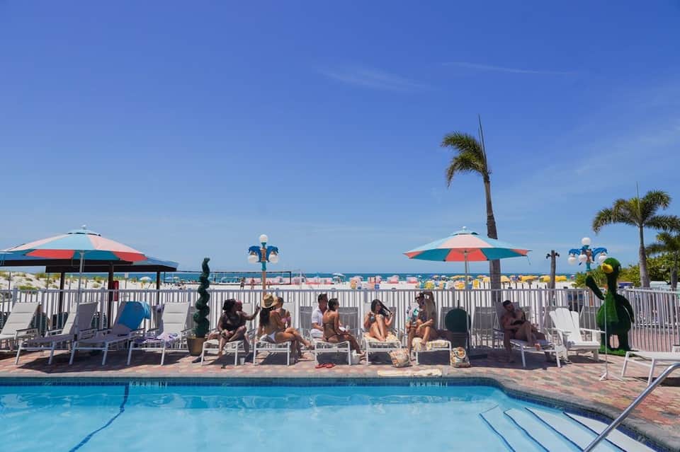 Resort pool with clear blue water, white railings, lounge chairs with umbrellas, and ocean view beyond