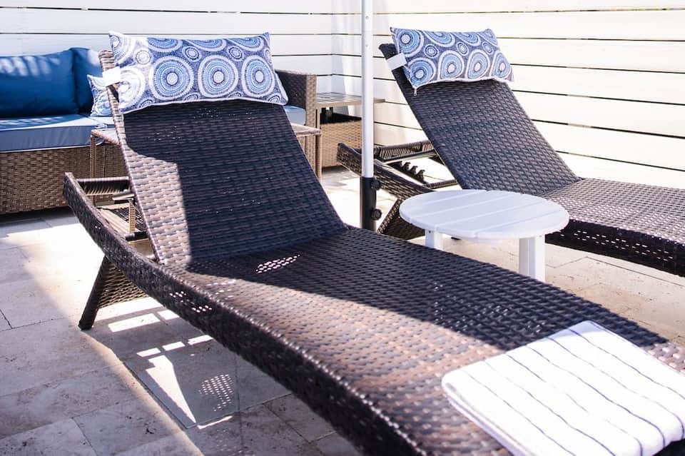 Close-up of woven lounge chairs with blue patterned pillows on a sunny deck