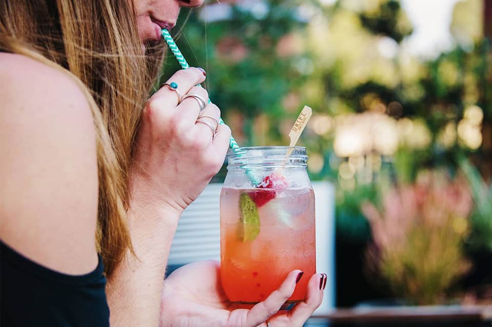 Woman drinking a colorful pink cocktail with fruit garnish in a garden setting