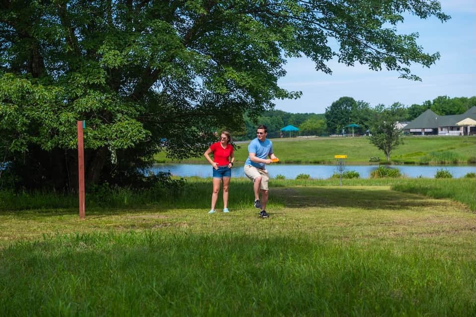 Two people jogging on grassy field beside river with resort facilities visible across water