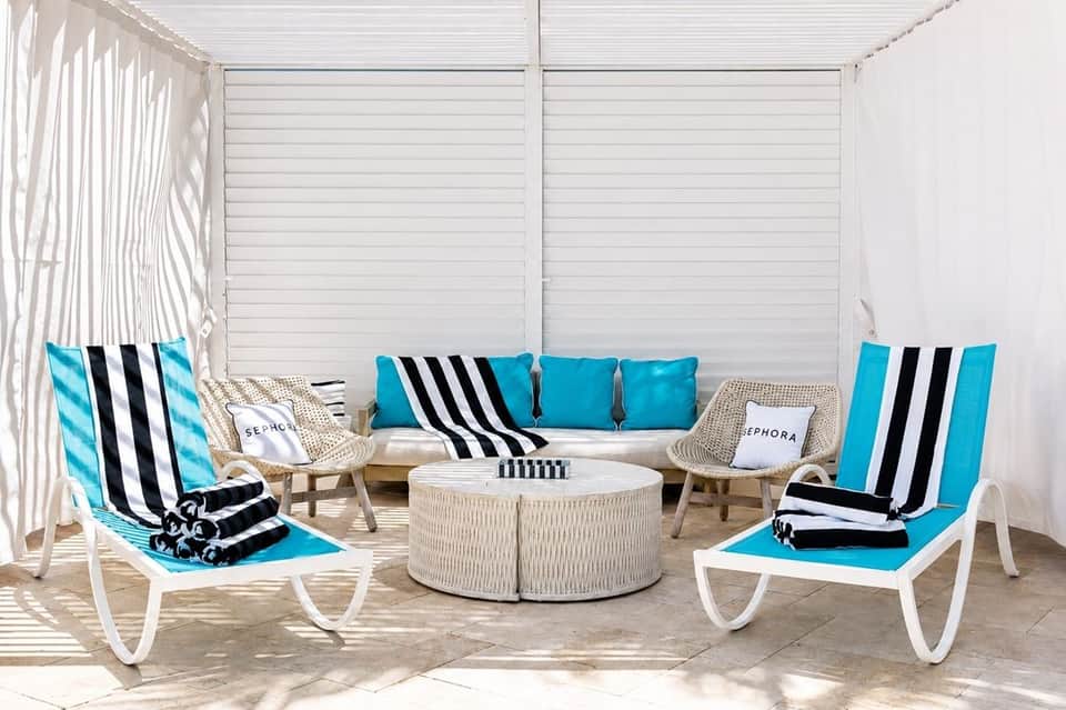 Luxury cabana lounge with striped cushions, turquoise accents, white privacy walls, and woven furniture