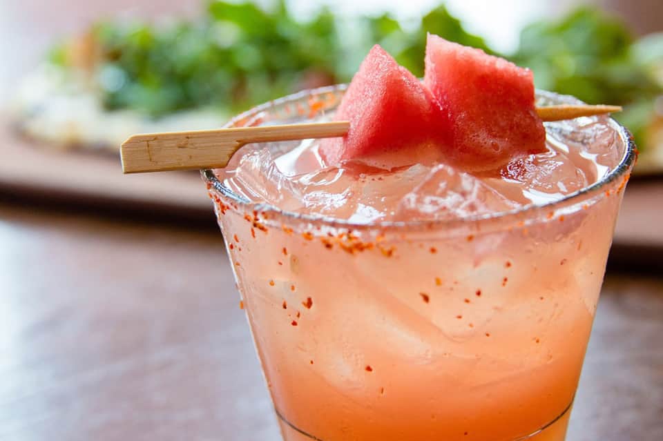 Tropical cocktail with watermelon garnish and spiced rim, served over ice