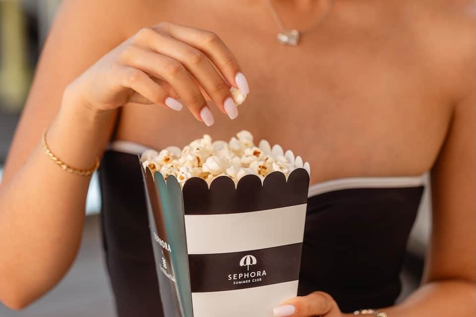 Woman's hands holding striped Sephora Summer Club popcorn container at poolside