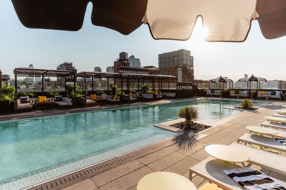 Rooftop pool deck with turquoise water, striped umbrellas, and city skyline view