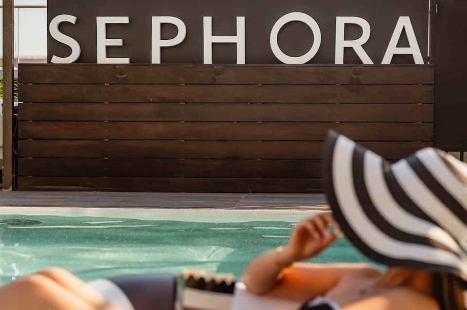 Sephora storefront with dark wooden exterior overlooking a turquoise pool and striped beach umbrella