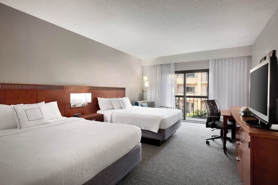 Hotel room with two queen beds, wooden headboard, flat-screen TV, and balcony access with city views