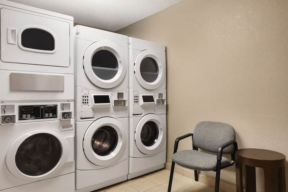 Laundry facility with stacked commercial washers, dryers, and gray upholstered seating chair