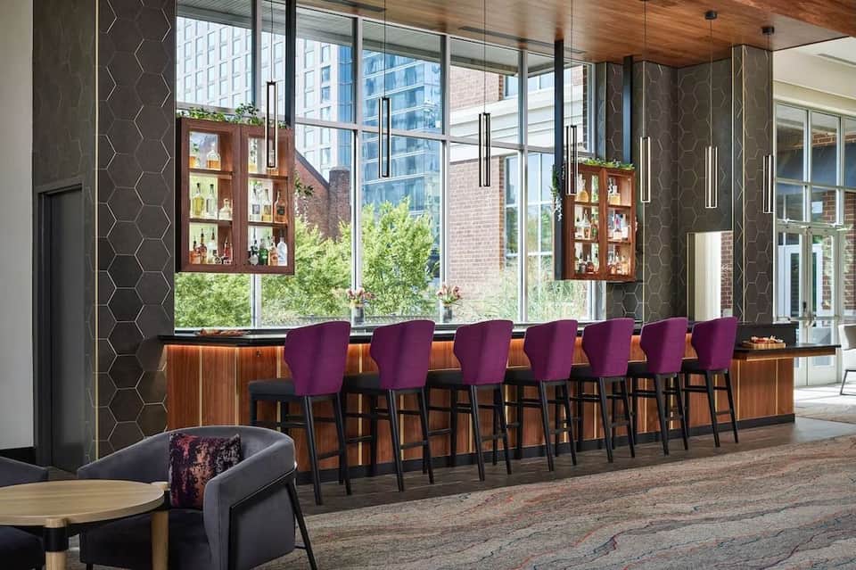 Modern hotel bar with purple bar stools, wooden cabinetry, large windows overlooking city buildings
