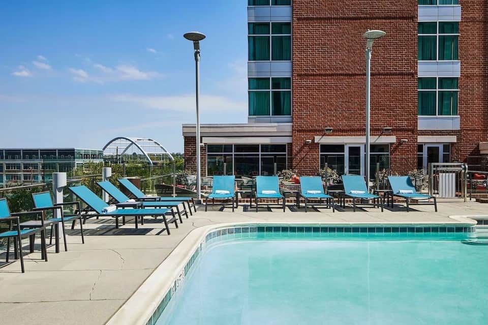 Rooftop pool with turquoise water, lounge chairs with blue cushions, brick building backdrop
