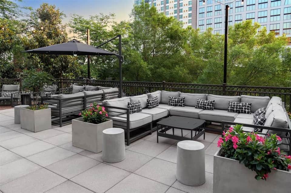Rooftop lounge with gray sectional sofa, black umbrella, planters with flowers, and city views