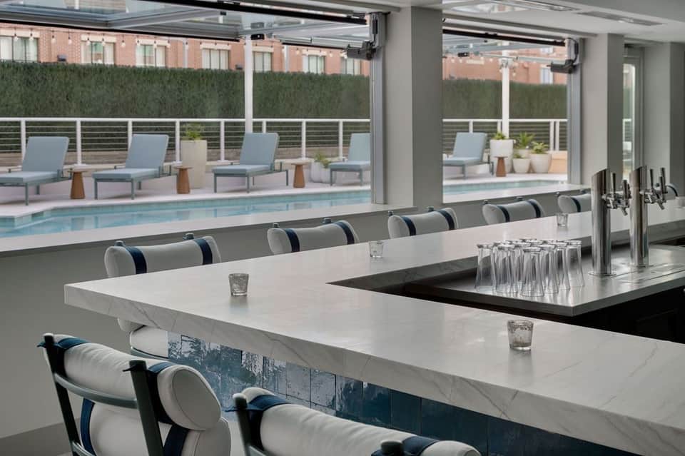 Indoor bar with view of outdoor pool through glass doors and lounge seating area