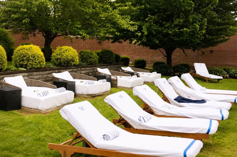 Array of white wooden lounge chairs on manicured lawn with topiary and brick walls