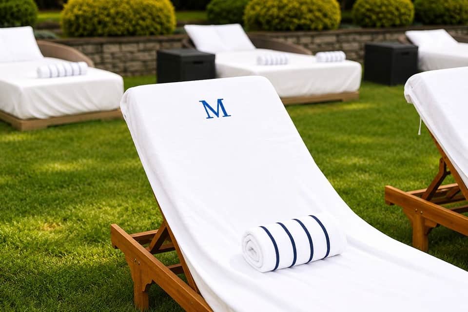 White monogrammed lounge chair with towel on manicured lawn, part of resort seating arrangement