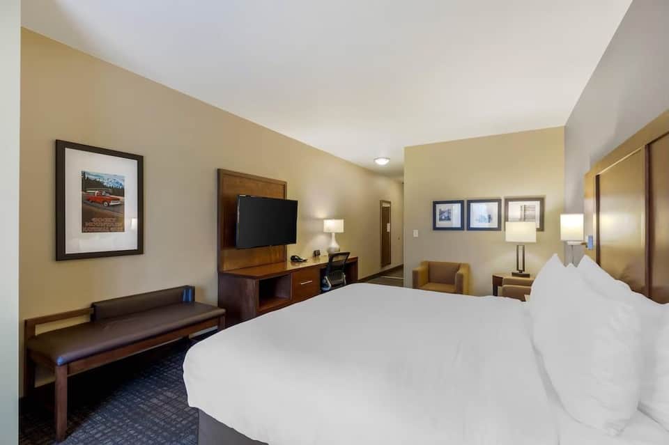 Hotel room with king bed, wood furniture, TV, armchair, and warm beige wall color