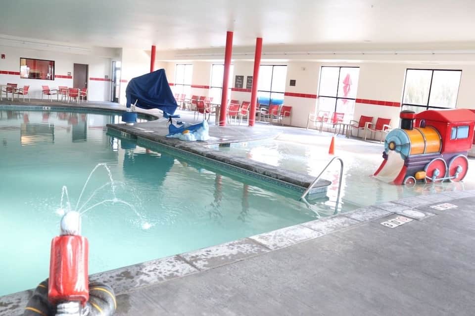 Indoor swimming pool with water features and red play equipment in brightly lit facility
