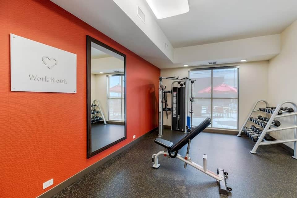 Fitness center with orange accent wall, exercise equipment, and city views through windows