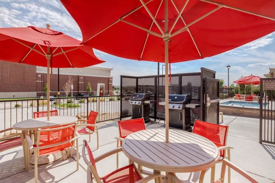 Rooftop patio with red umbrellas, dining tables, grills, and pool in background at dusk