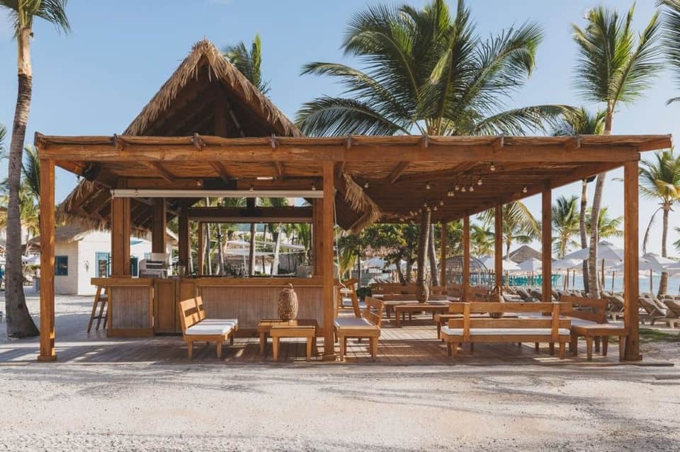 Beach cabana with thatched roof, wooden seating area, and palm trees