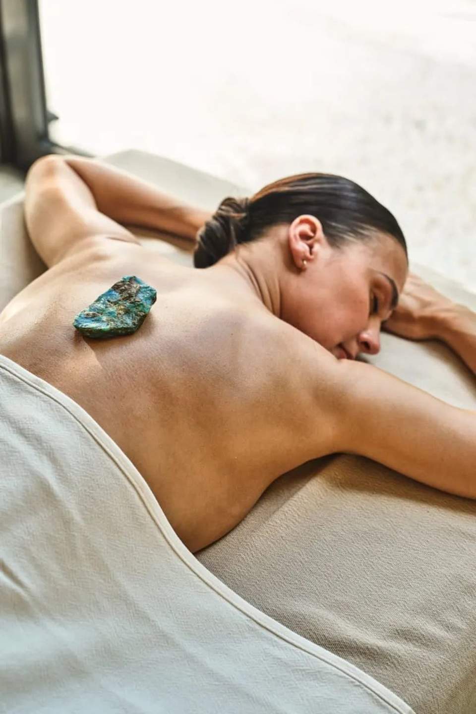 Woman receiving spa treatment with turquoise stone on her back in treatment room