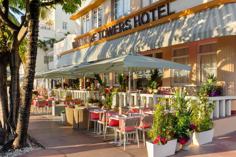 Historic Victor Towers Hotel beachfront entrance with outdoor dining, umbrellas, and tropical landscaping