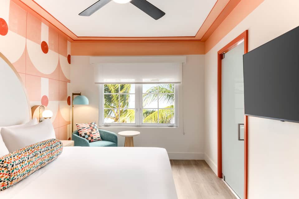 Hotel bedroom with coral ceiling trim, patterned bedding, and coastal view window
