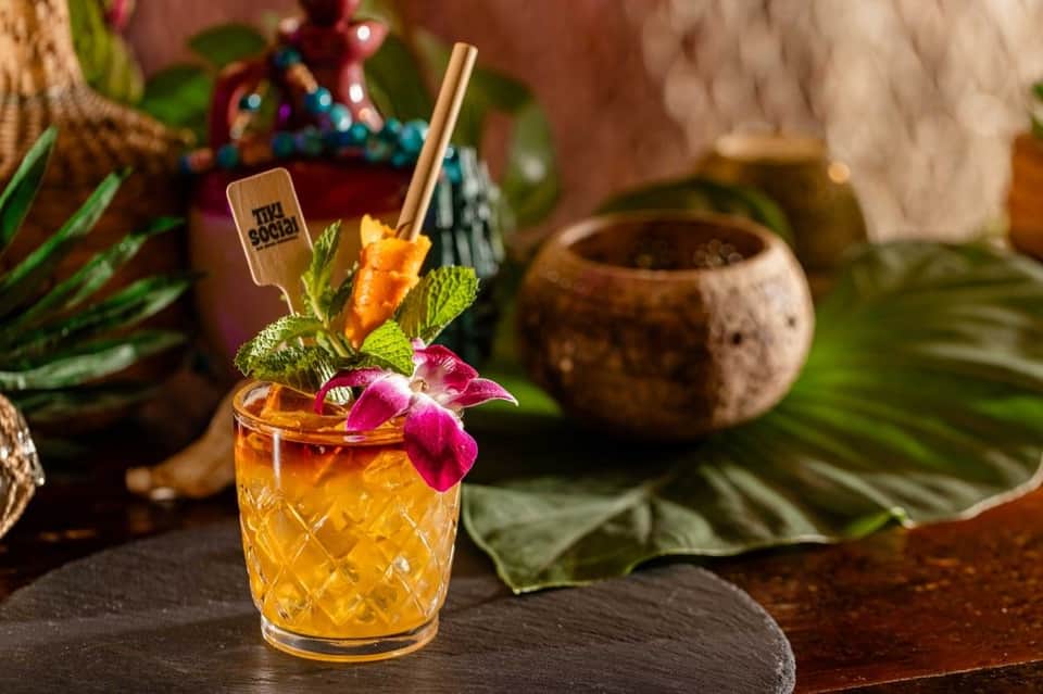Colorful tropical cocktail with orchid flower garnish and wooden bar stir stick