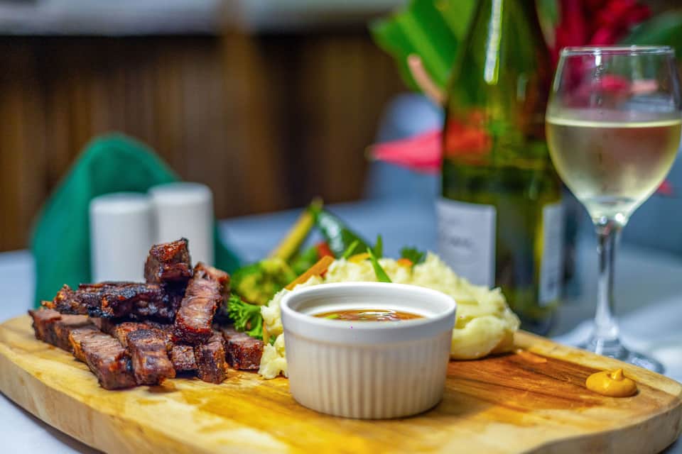 Plated grilled meat skewers with sauce, fresh vegetables, and white wine glass