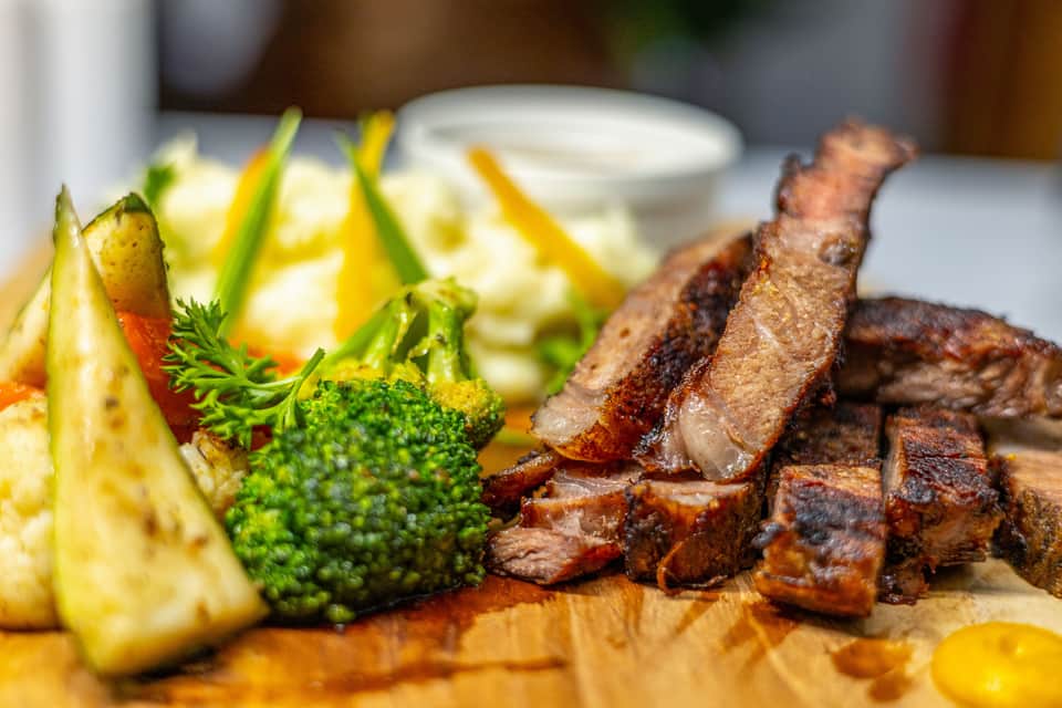 Seared steak strips with fresh broccoli and pineapple on wooden cutting board