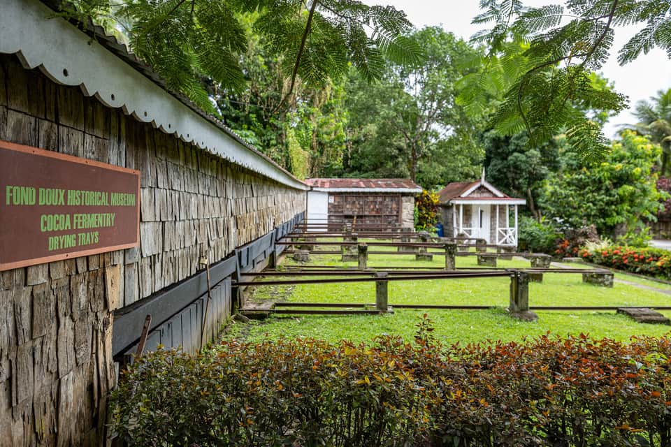 Fond Doux Historical Museum with wooden cocoa fermentry building, drying trays, and manicured grounds surrounded by lush vegetation