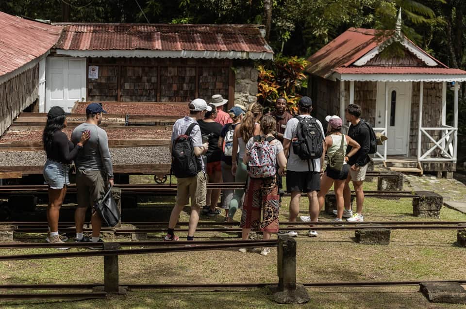Group of tourists gathered at a colonial-era village site with corrugated metal-roof buildings