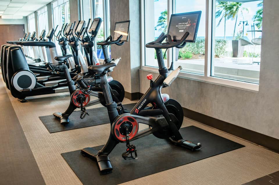 Indoor cycling studio with stationary bikes and elliptical machines overlooking tropical landscape