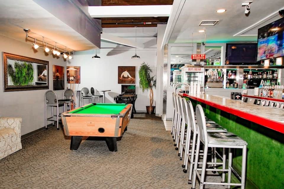 Entertainment space with pool table, green felt, bar with red top edge, white bar seating, and game area