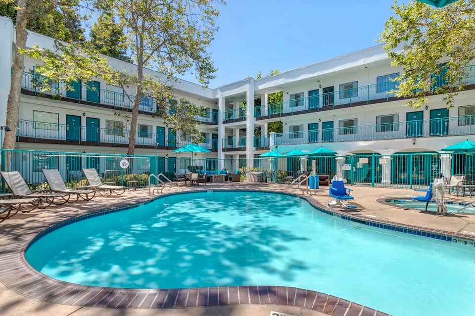 Curved resort swimming pool with bright turquoise water, lounge chairs, turquoise umbrellas, and white balconied buildings