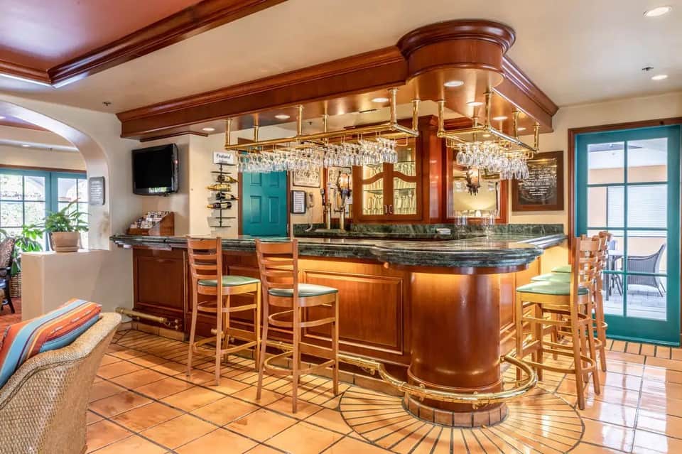 Elegant curved bar with wood cabinetry, brass fixtures, crystal chandeliers, and turquoise accents