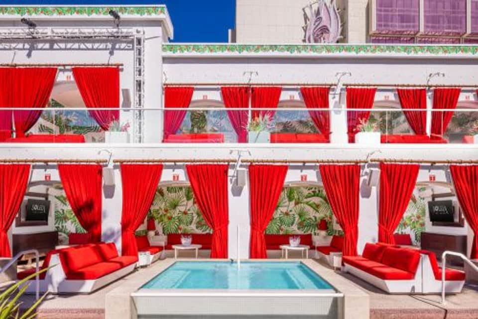 Red cabana-style seating areas with curtains flanking a rectangular pool on a modern terrace