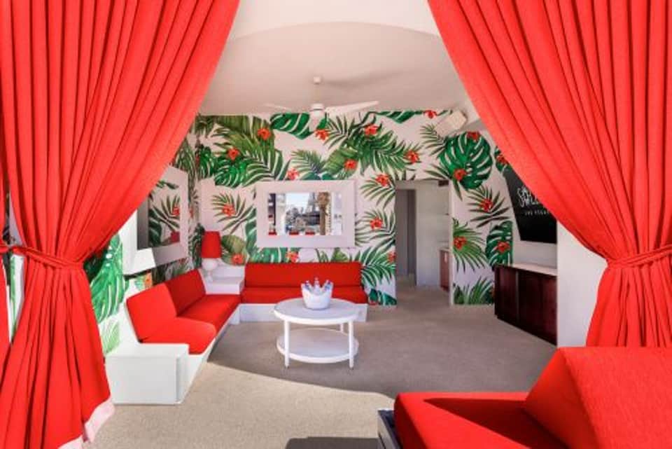 Modern hotel lounge with tropical leaf wallpaper, red curtains, white furniture, and red accent chairs framing the entrance