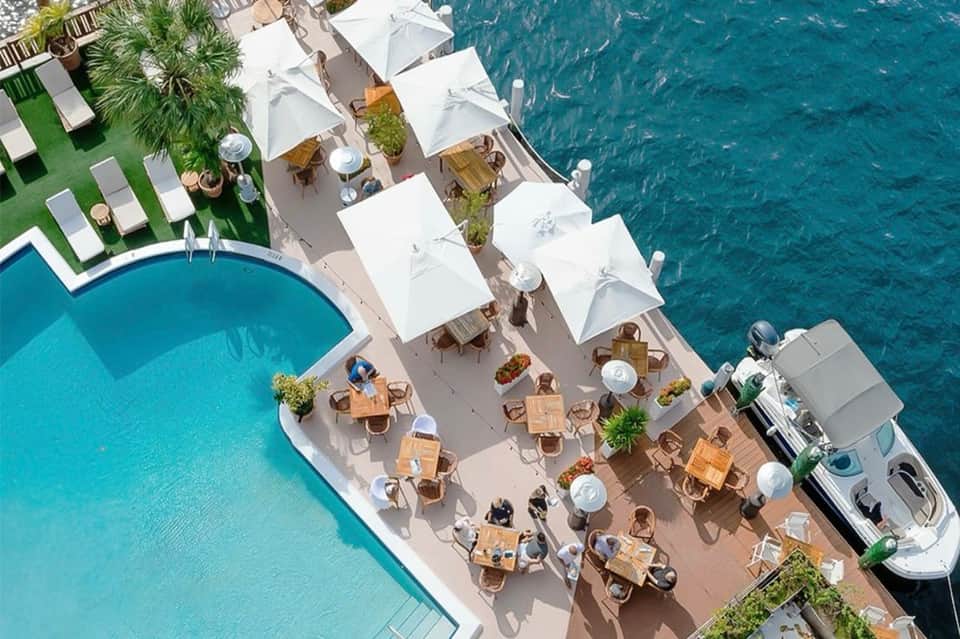 Aerial view of resort with pool, white umbrellas, lawn seating, and turquoise ocean